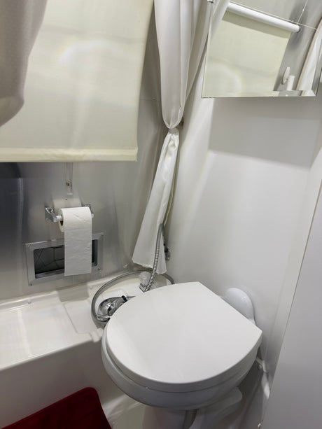 Compact RV rental bathroom: toilet, shower, and toilet paper dispenser over tub, with a tied-back shower curtain.
