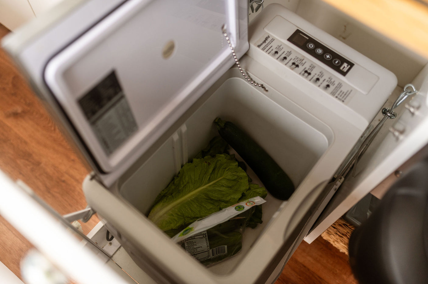 Inside an RV rental's portable refrigerator, holding fresh lettuce and zucchini for travel meals.