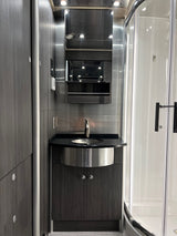 Modern RV rental bathroom: sleek vanity with sink, mirror, and curved shower enclosure.