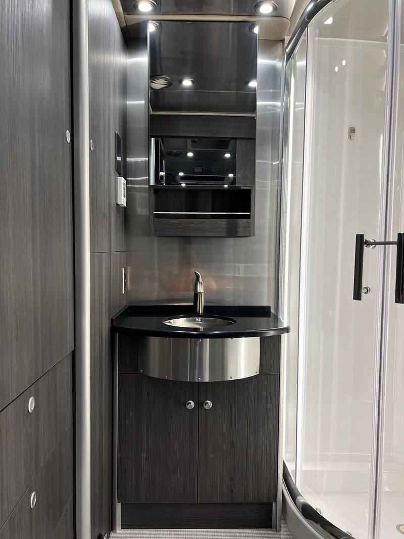 Modern RV rental bathroom: sleek vanity with sink, mirror, and curved shower enclosure. — photo 16