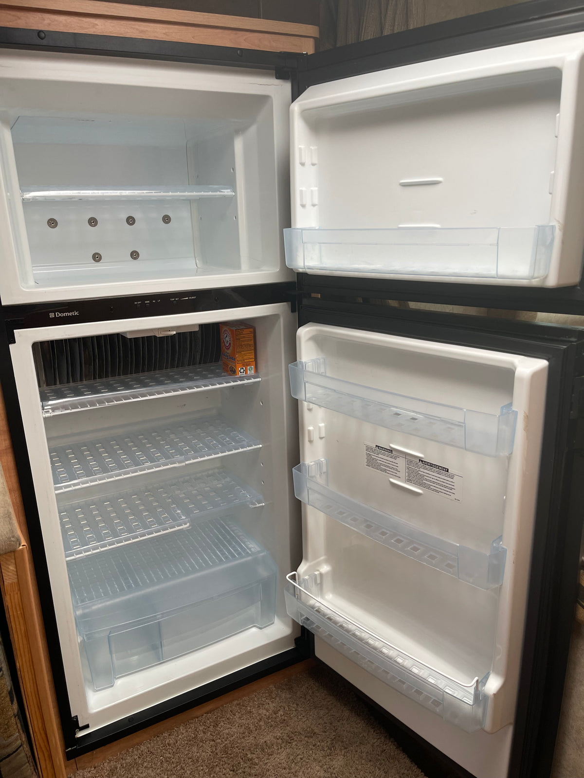 Clean, empty Dometic RV rental refrigerator interior showing shelves, door bins, and control panel. A box of baking soda sits inside. — photo 6