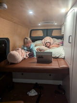 Two children in a cozy RV rental bed, one in a bunny hat, watch a laptop. Perfect for family travels.