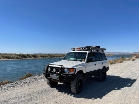 Custom white SUV parked by a river, ready for overlanding. An ideal RV rental for off-road adventure and exploration.