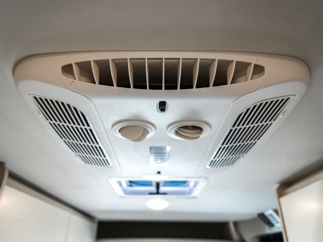 RV rental interior: A white ceiling-mounted air conditioner with vents and circular controls for passenger comfort.