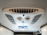 RV rental interior: A white ceiling-mounted air conditioner with vents and circular controls for passenger comfort.