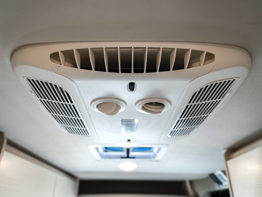 RV rental interior: A white ceiling-mounted air conditioner with vents and circular controls for passenger comfort.