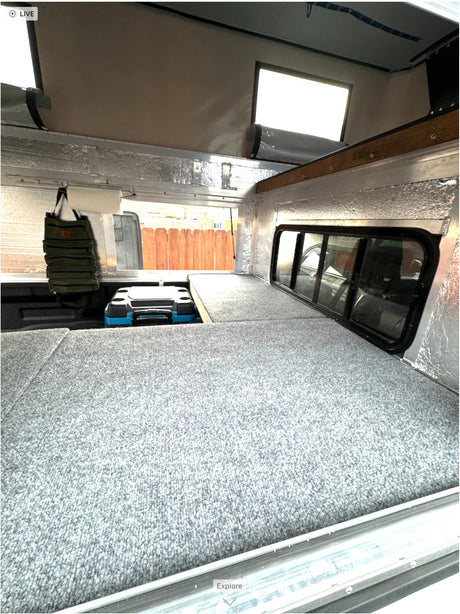 Cozy truck camper interior featuring a gray bed platform, cooler, and insulated walls. Ideal for an rv rental adventure.