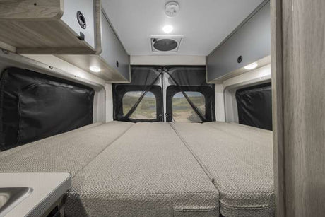 Spacious RV rental interior features a comfortable bed, overhead cabinets, and scenic views through rear windows.