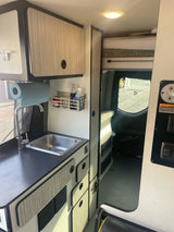 Compact RV rental interior featuring a practical kitchen area, modern cabinets, and comfortable sleeping space.