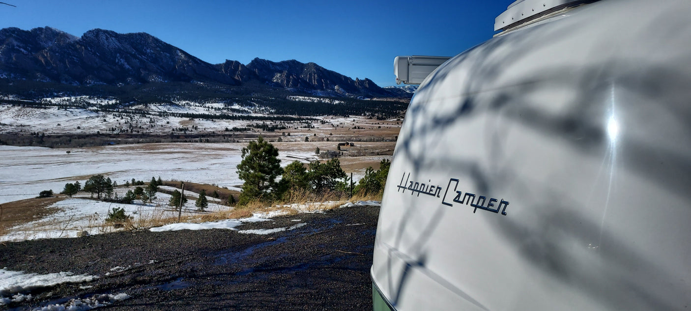 Enjoy an RV rental adventure: a Happier Camper travel trailer overlooking the snowy Boulder Flatirons.
