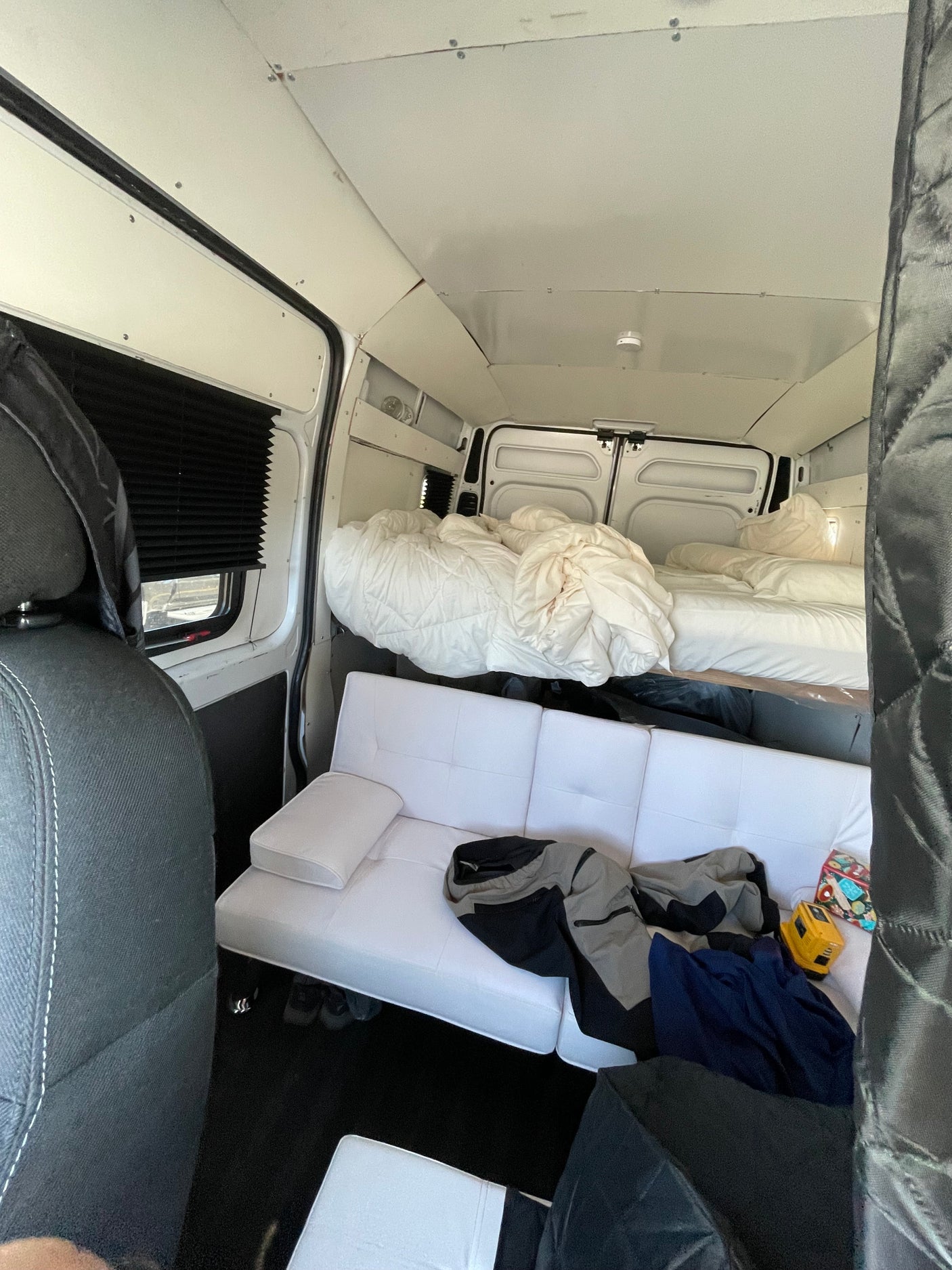 Inside an RV rental camper van with a cozy bed, white sofa, and window blinds. Ready for adventure!