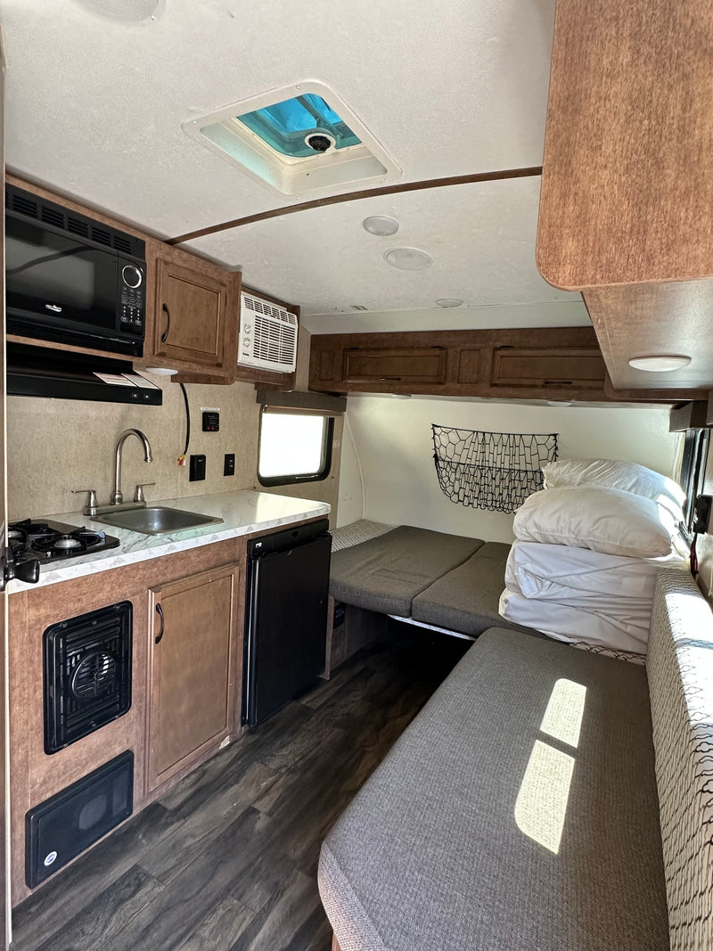 Compact RV rental interior featuring a kitchenette, convertible sleeping area, overhead AC, and smart storage solutions. — photo 4