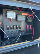 Essential RV rental power control: a panel with battery isolator, fuses, switches, 12V/USB outlets, and Renogy monitor.