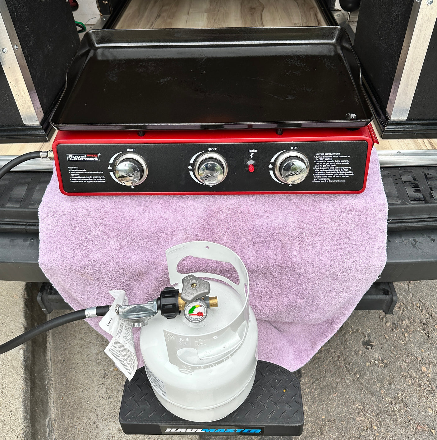 RV rental outdoor cooking setup: Red gas griddle & white propane tank on step, ready for camping meals.