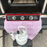 RV rental outdoor cooking setup: Red gas griddle & white propane tank on step, ready for camping meals.