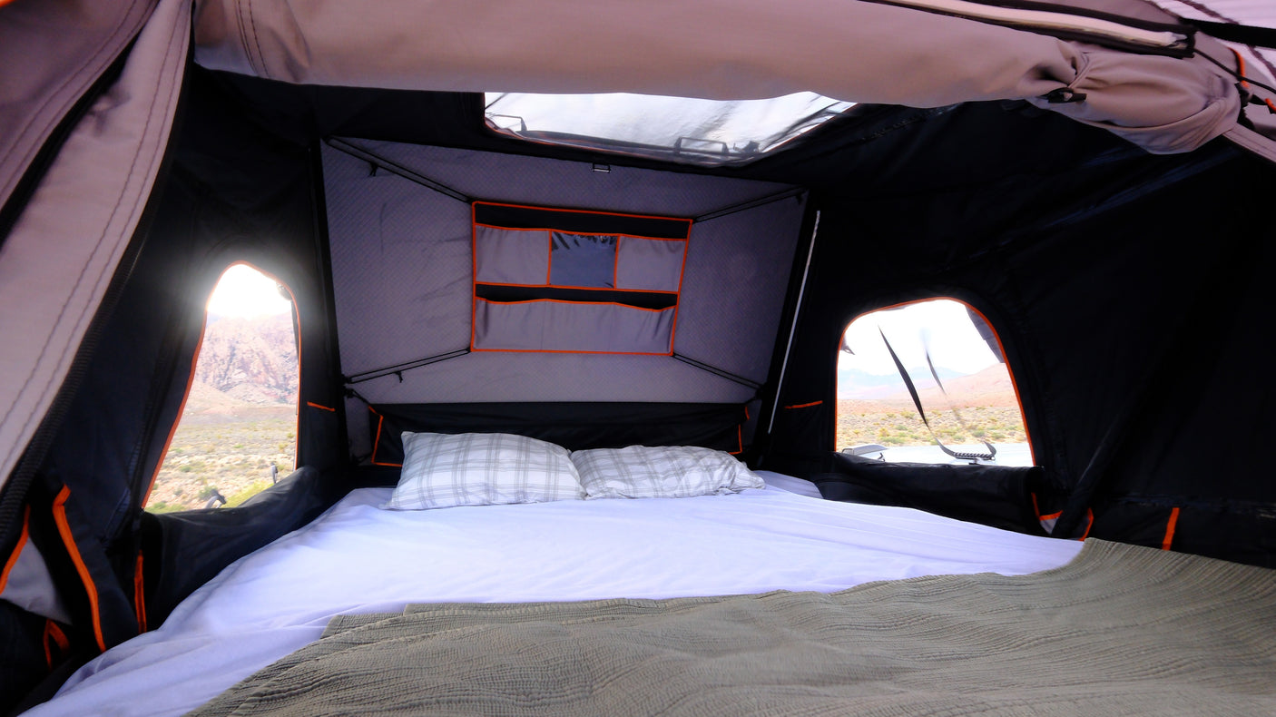 Cozy interior of an RV rental roof-top tent with a bed and scenic mountain views from the windows.