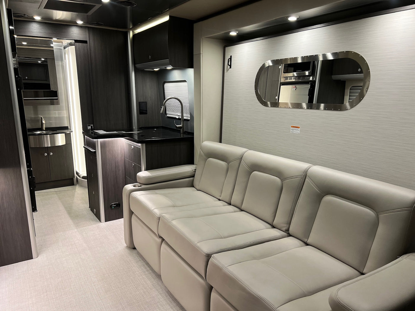 Explore this stylish rv rental interior, featuring a comfortable sofa, modern kitchen area, and mirror reflecting appliances. — photo 18