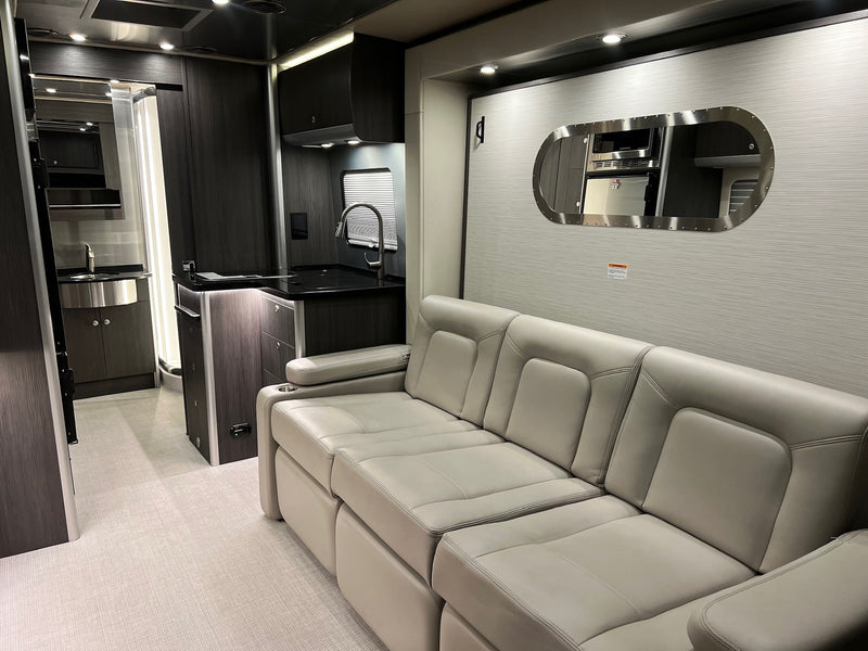 Explore this stylish rv rental interior, featuring a comfortable sofa, modern kitchen area, and mirror reflecting appliances. — photo 18