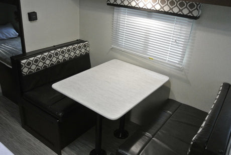 **RV rental**'s compact dinette area, featuring a white table, patterned bench seating, and window blinds.
