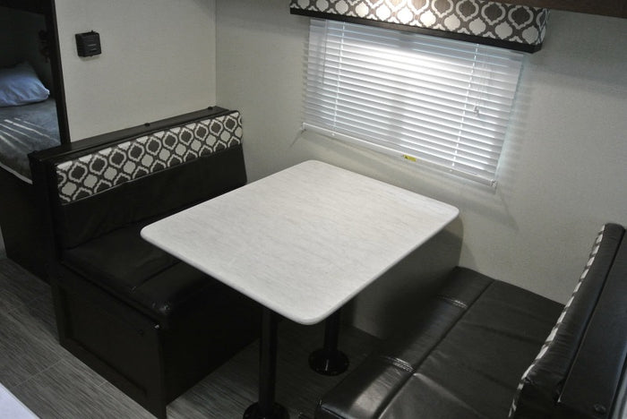 **RV rental**'s compact dinette area, featuring a white table, patterned bench seating, and window blinds.
