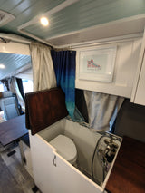 Inside an RV rental: a compact, functional bathroom with a toilet, shower, and artistic touches like a sneaker print.