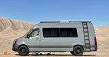 A modern gray Sprinter RV rental stands ready for adventure in a vast desert landscape with mountains.
