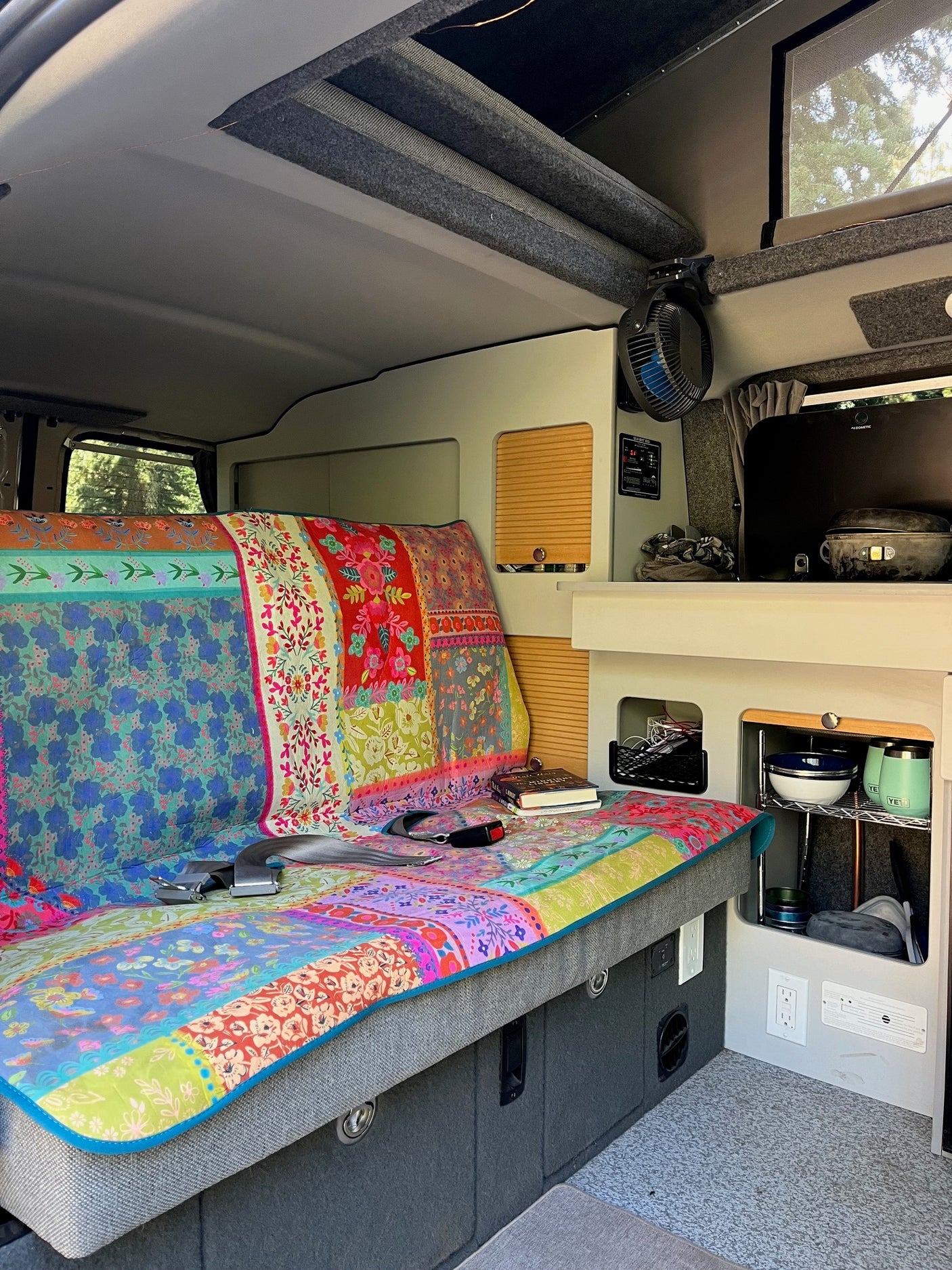 Cozy RV rental interior with colorful bedding, compact kitchen, and overhead storage for comfortable travel.