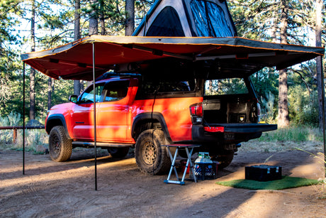 Red Toyota Tacoma truck with deployed rooftop tent and awning. A versatile overland camp setup, an alternative to an RV rental.