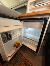 RV rental's compact fridge is open, showcasing beverages and a freezer, a convenient amenity for your adventures.