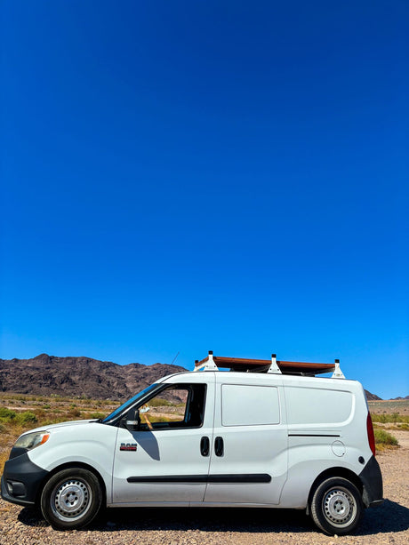White Ram ProMaster City van with roof deck, parked on a dirt road in a desert mountain landscape. Great for an RV rental.