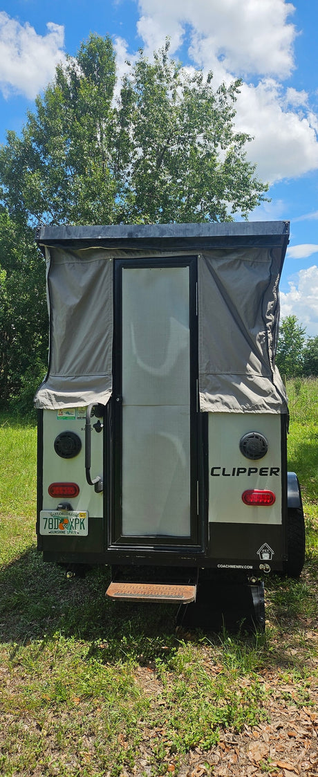 Rear view of a pop-up Clipper camper, great for an RV rental adventure, parked in a grassy spot under a blue sky.
