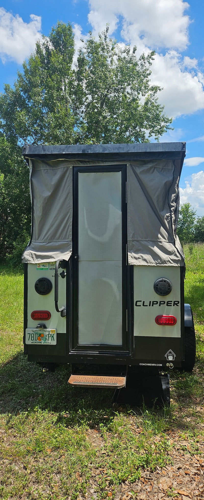 Rear view of a pop-up Clipper camper, great for an RV rental adventure, parked in a grassy spot under a blue sky. — photo 7