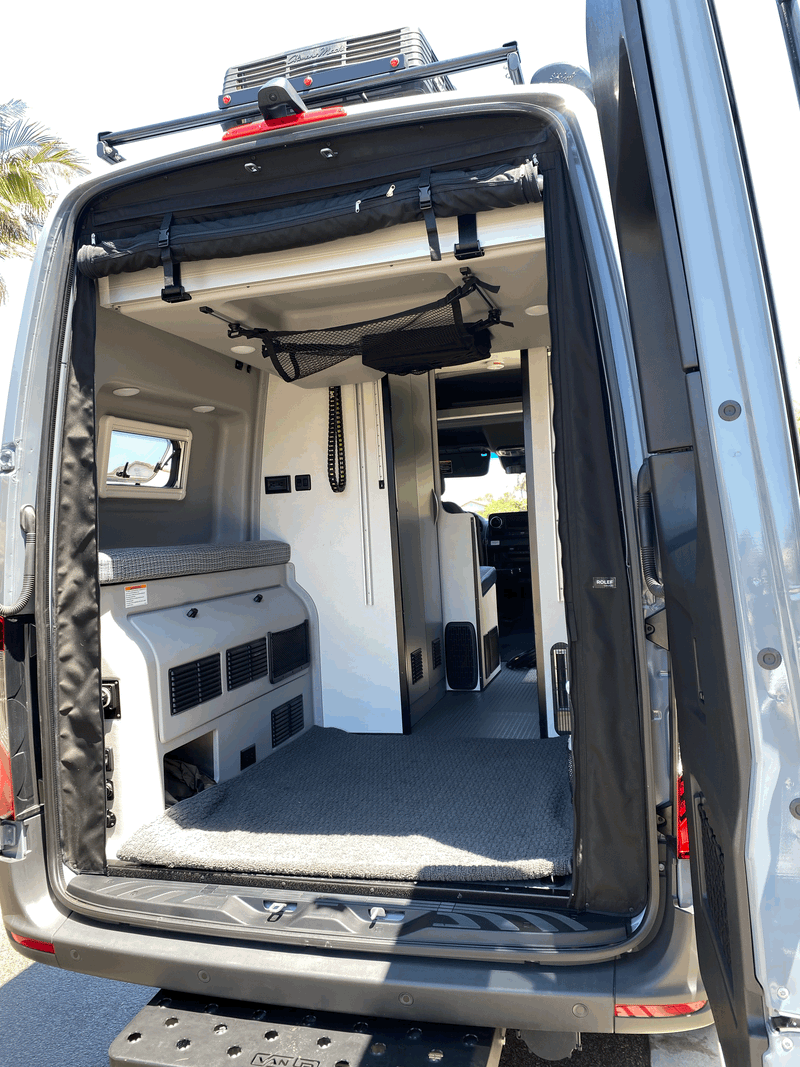RV rental camper van interior from back: features elevated bed with cushion, built-in storage, and overhead mesh netting. — photo 7