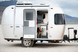 A tan dog stands inside a silver Airstream Bambi travel trailer, parked in the desert. Ideal for your next RV rental trip!