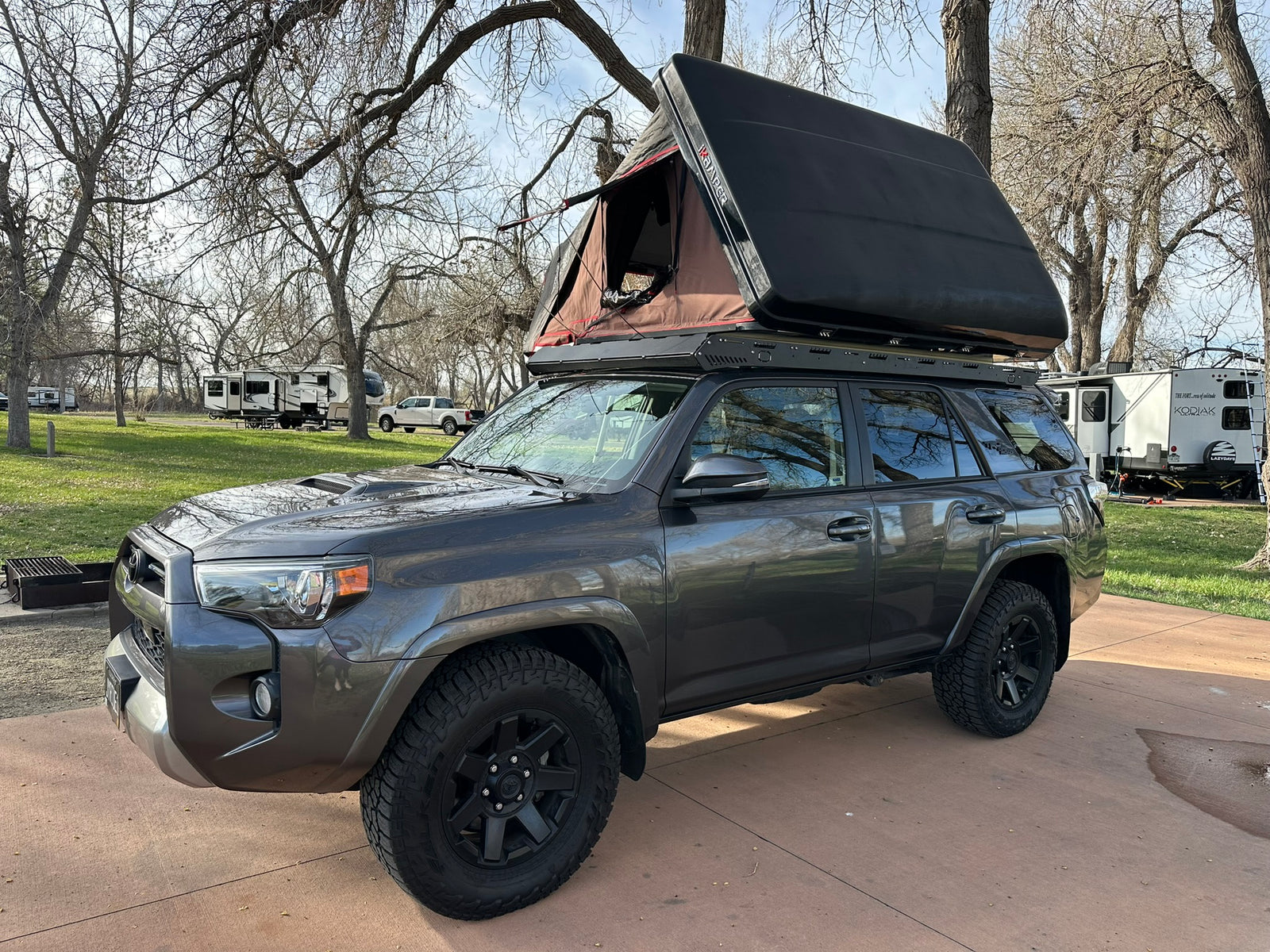 This grey SUV with a rooftop tent is ready for camping at an RV park, a unique alternative to an RV rental.
