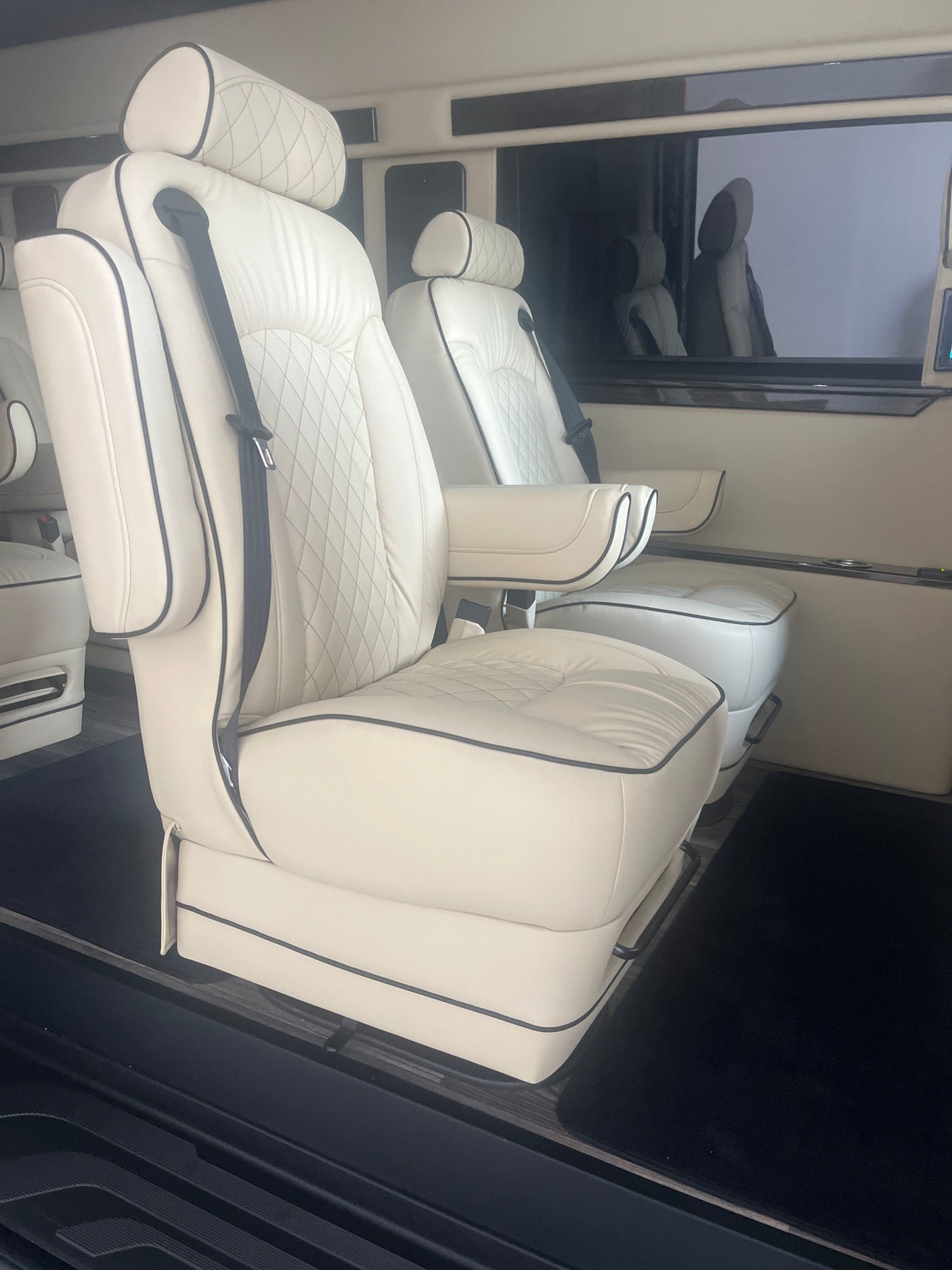 Luxury RV rental interior with plush cream leather captain's chairs, black piping, and diamond quilting. Ideal for comfortable travel.