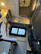 Inside an RV rental: comfortable quilted seats, overhead cabinets & lights, controls, and a roof vent providing natural light.