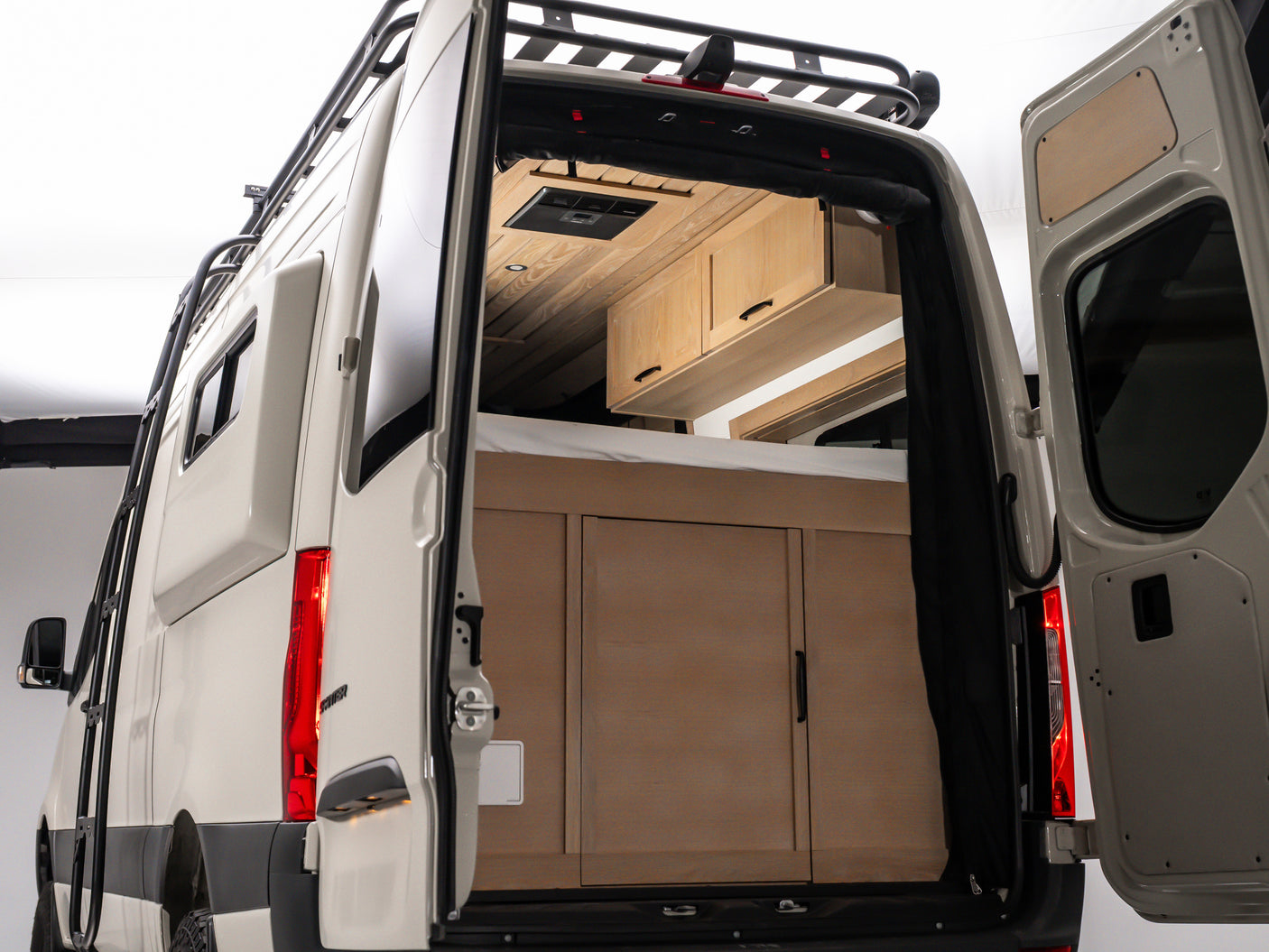 Rear view of a spacious RV rental interior with custom wooden cabinetry, bed, and ventilation, perfect for journeys.