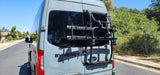 Rear view of a light blue Mercedes-Benz Sprinter RV rental with a bike rack, parked on a sunny residential street.