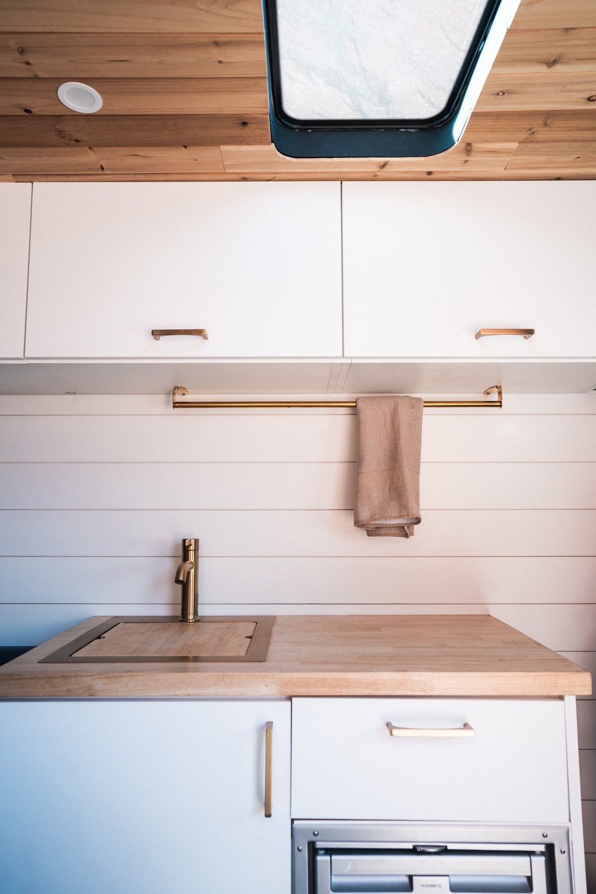 This bright RV rental kitchen showcases white flat-panel cabinets, warm wood ceiling and countertop, brass faucet, and a covered sink. — photo 6