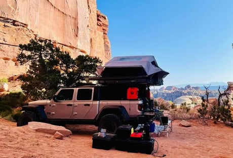Jeep Gladiator with rooftop tent deployed, a unique RV rental for overlanding. Camping in a vast red rock canyon.