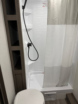 Experience this clean RV rental bathroom with a shower, wavy-textured wall, striped curtain, toilet, and convenient shelving.