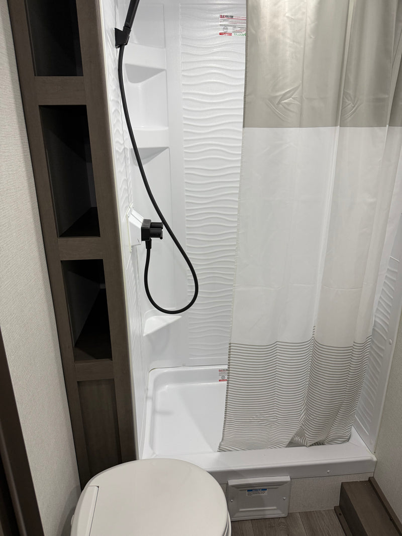 Experience this clean RV rental bathroom with a shower, wavy-textured wall, striped curtain, toilet, and convenient shelving. — photo 4