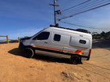 Silver Mercedes Sprinter camper van, with a retro stripe, parked on a dirt shoulder. An ideal RV rental for outdoor adventures.