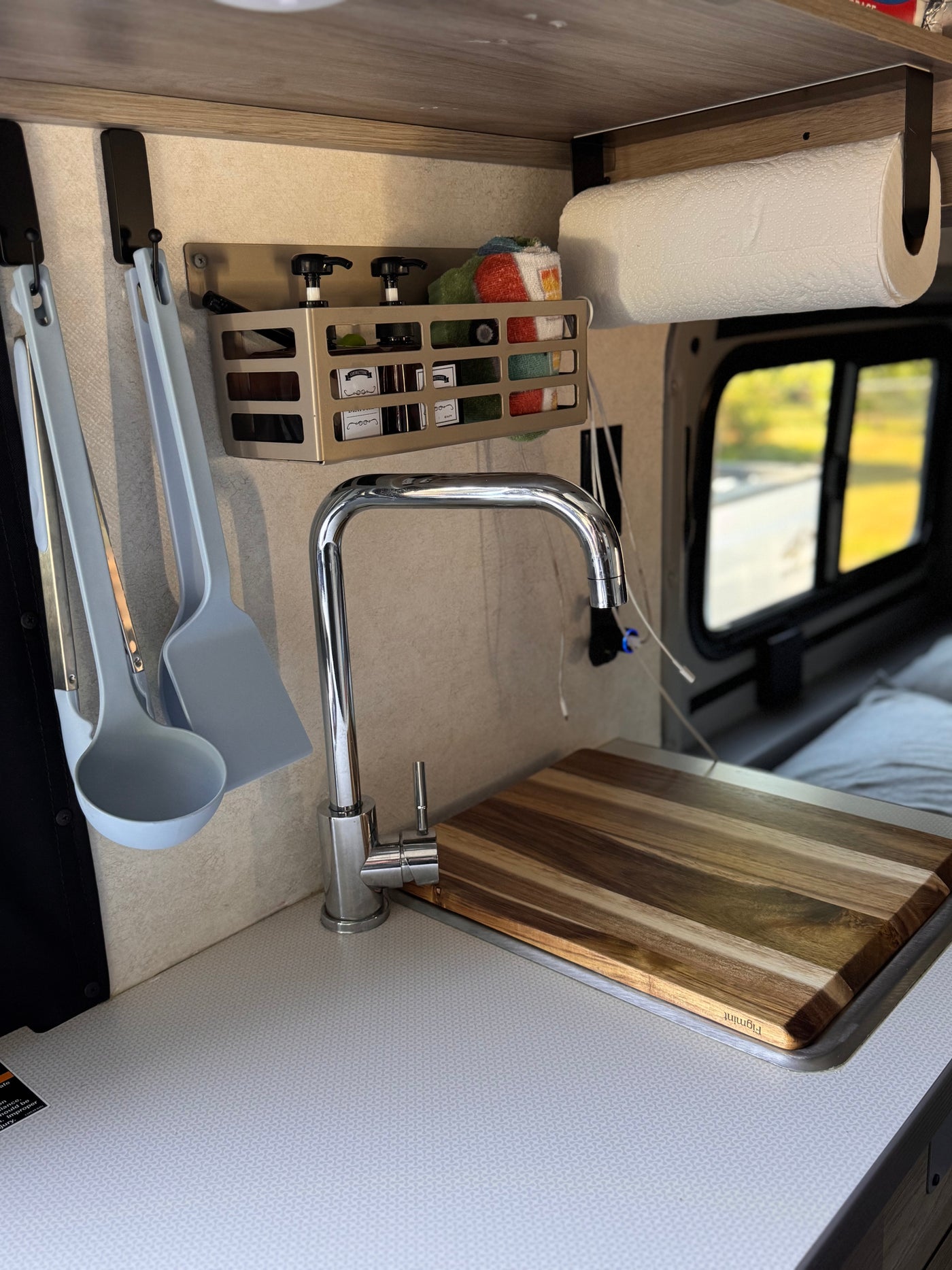 Compact RV rental kitchen with modern faucet, smart storage, and cutting board over the sink. Ideal for travel. — photo 10