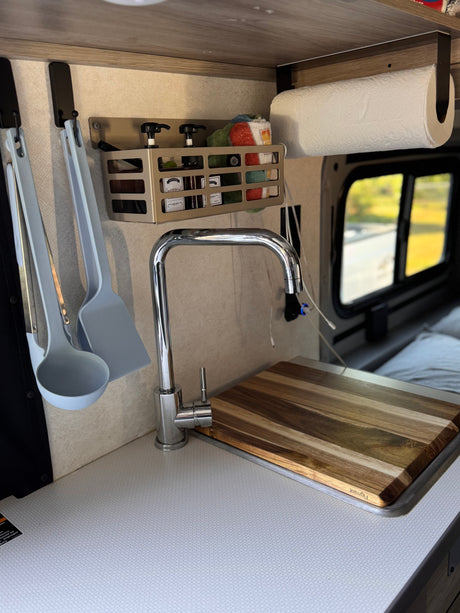 Compact RV rental kitchen with modern faucet, smart storage, and cutting board over the sink. Ideal for travel.