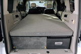 View inside an RV rental camper van, revealing a compact bed, under-bed storage, and Dometic cooler.