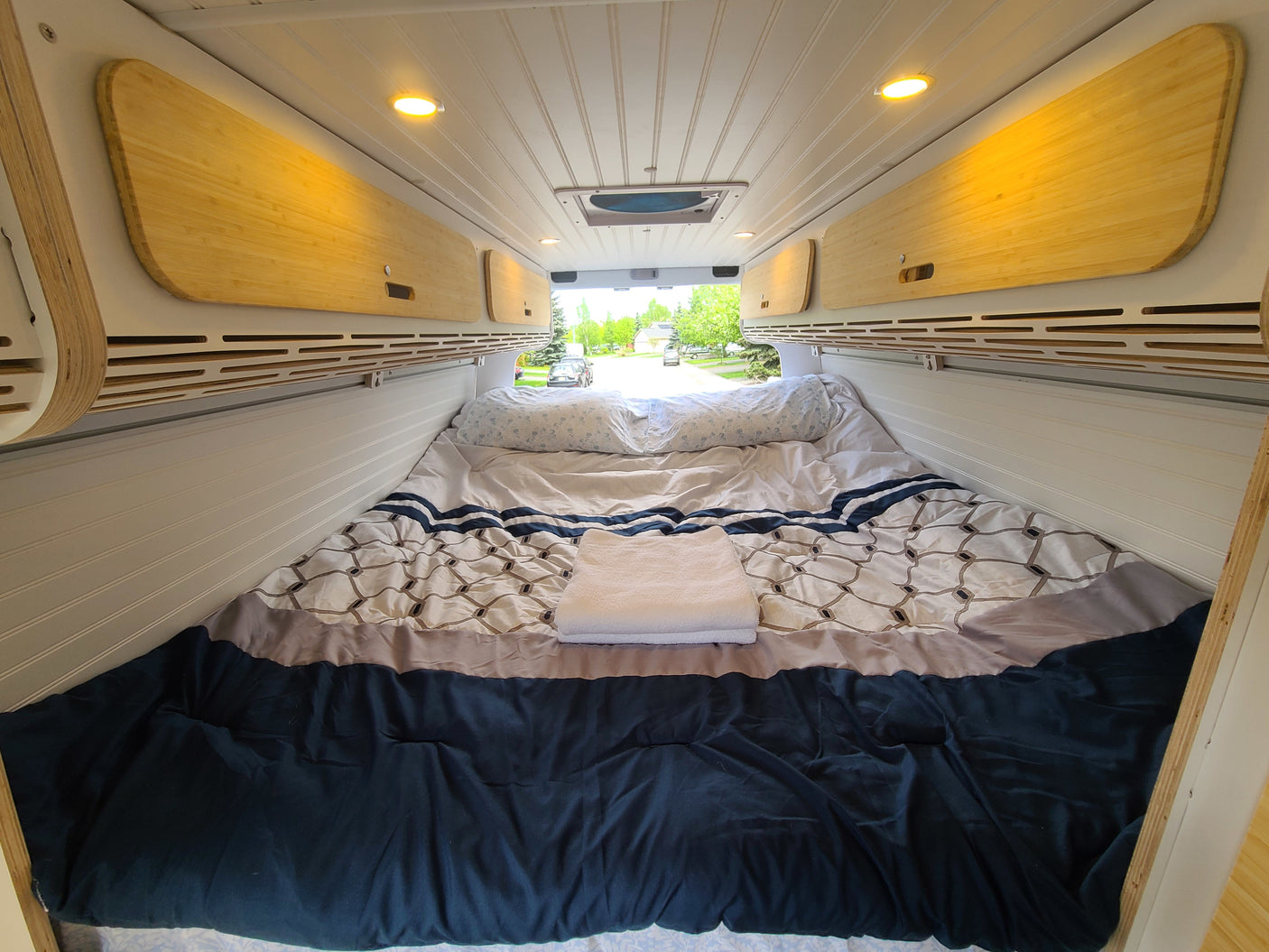 RV rental bedroom: cozy bed, warm bamboo overhead storage, and bright ceiling lights for comfort.