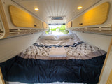 RV rental bedroom: cozy bed, warm bamboo overhead storage, and bright ceiling lights for comfort.