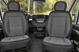 Spacious RV rental cabin featuring comfortable dark grey fabric seats, a modern dashboard, and a view of a forested road.